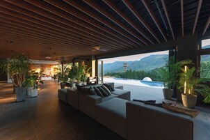 Un interior moderno con un amplio sofá modular, plantas en macetas y vistas a las montañas.