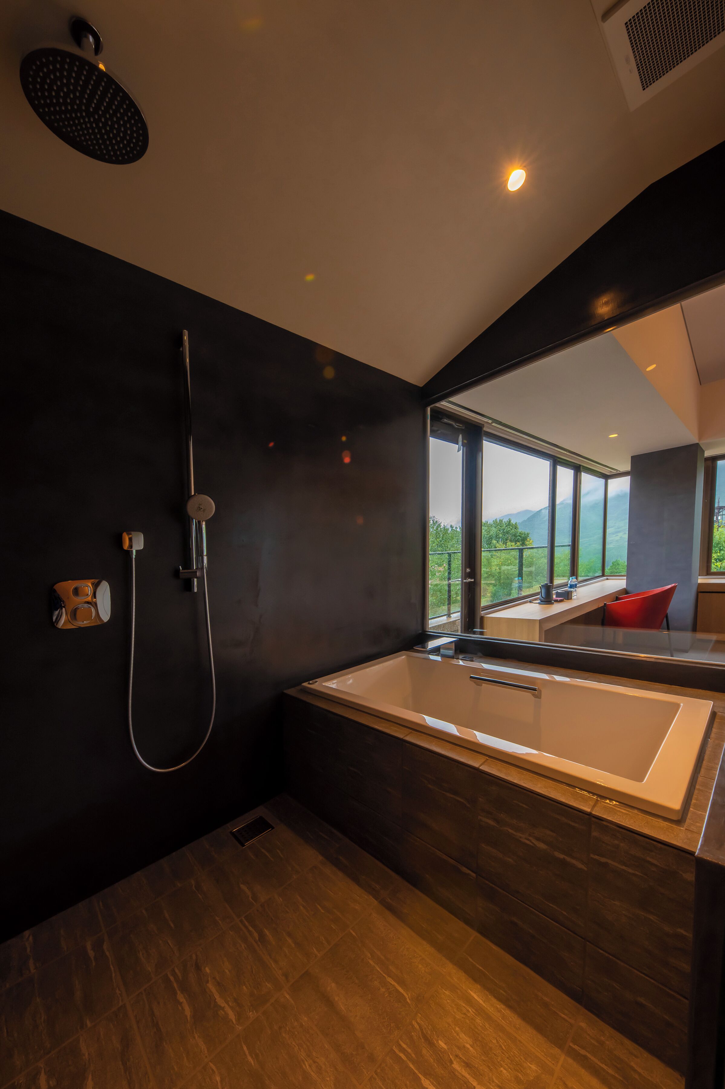 Un baño moderno con una bañera grande, ducha y vistas a un paisaje montañoso a través de amplios ventanales.