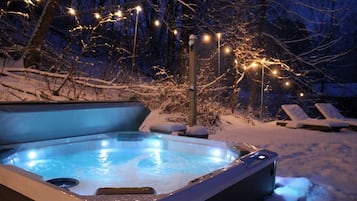 Uma banheira de hidromassagem rodeada de neve, com espreguiçadeiras e luzes de Natal.
