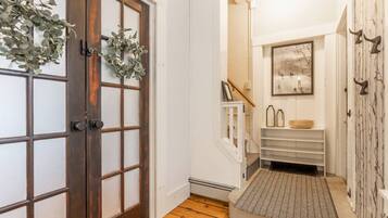 Um corredor com porta de madeira, parede branca, escada, quadro emoldurado e um pequeno prateleira com objetos decorativos.