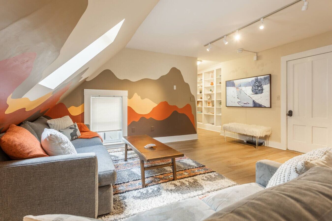 Een loft-achtige woonkamer met een schuine plafond, een zithoek, een salontafel, een boekenkast en een schilderij aan de muur.
