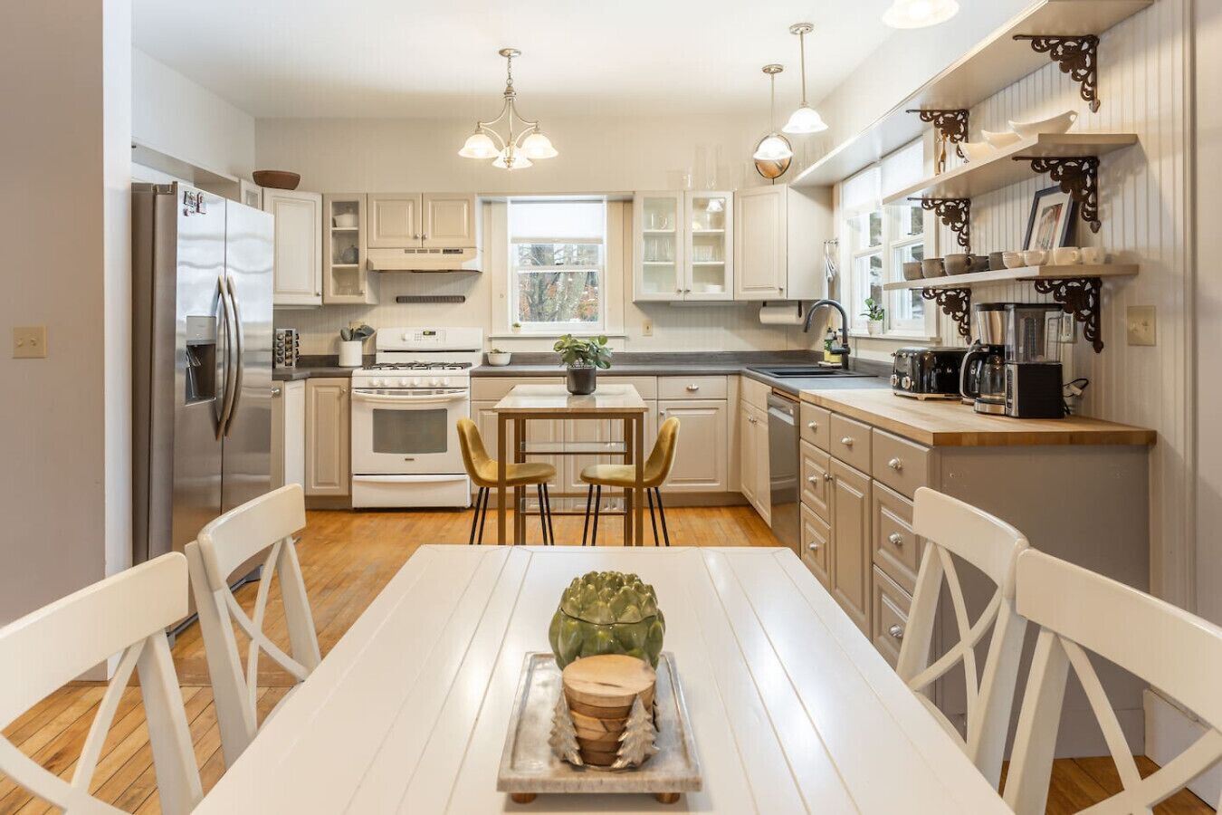Una cocina moderna con armarios blancos, una mesa de comedor con sillas, un refrigerador, una estufa y una cafetera.