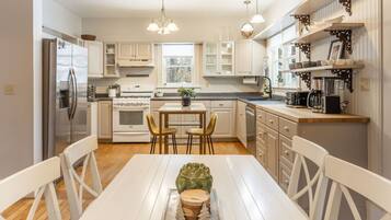Una cocina moderna con armarios blancos, una mesa de comedor con sillas, un refrigerador, una estufa y una cafetera.