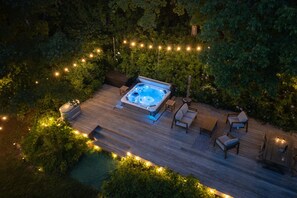 Vista aérea de un jacuzzi rodeado de mobiliario de madera y luces colgantes, situado en un exuberante jardín.