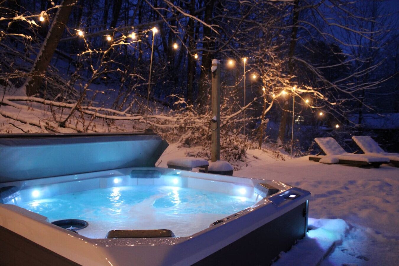 Un jacuzzi rodeado de nieve, con sillones reclinables y luces colgantes.