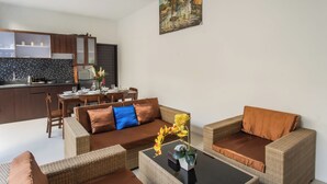 Un espace de vie moderne comprenant un canapé, une table basse et une table à manger. On aperçoit une cuisine à l’arrière-plan.