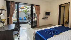 Une chambre d’hôtel comprenant un lit, un bureau, une chaise, une télévision et une porte-fenêtre coulissante donnant sur un espace extérieur.