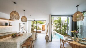 Et moderne køkken med bordplade i marmor, træbøtter og et spiseområde med udsigt til poolen.