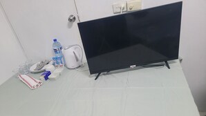 A table with a white tablecloth, a black TV, a water bottle, a milk carton, a plate with cutlery, and a folded red and white napkin.