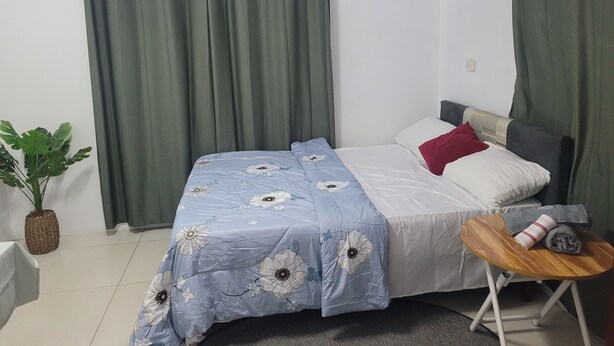 A bedroom with a bed, green curtains, a small table with a towel, and a potted plant.