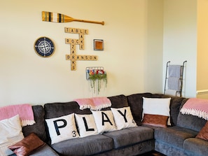 A cozy living room with a sectional sofa, a wall clock, a wooden bat, a crossword puzzle, and a hanging plant.