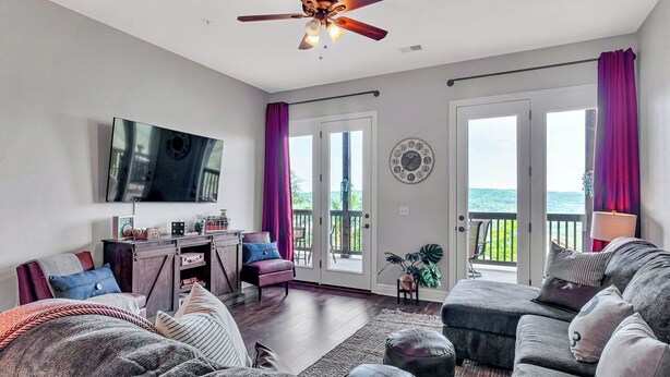 A living room with a ceiling fan, a flat-screen TV, a desk with a chair, a sofa, and a large window with curtains. - Stay & Play! Right next to SDC + Waffles, Games, Hottub, Pool, Outdoor Movies! (Branson)