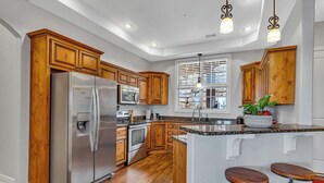 A modern kitchen with wooden cabinets, stainless steel appliances, and a central island with stools. - Stay & Play! Right next to SDC + Waffles, Games, Hottub, Pool, Outdoor Movies! (Branson)