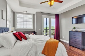 Ein Schlafzimmer mit Bett, Deckenventilator, Fernseher, Fenster mit Jalousien und einem Balkon mit Aussicht.