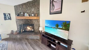 A living room with a stone fireplace, a flat-screen TV on a wooden stand, and a framed picture above the fireplace. - Summit Sanctuary of MeadowRidge. Great space and great location! (Fraser)