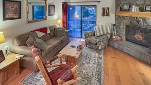 Un salon chaleureux avec une cheminée en pierre, une table basse en bois, un fauteuil rouge et un canapé.