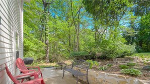 A patio with red chairs and a table, surrounded by a stone wall and greenery.