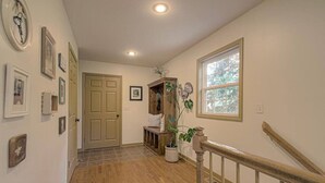 A hallway with wooden flooring, a door, a bench, and a window with a view of trees.