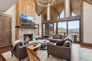 A spacious living room with a stone fireplace, leather sofas, and a large TV. - 3BR LUX Cabin w Firepit, Game Loft + Scenic Views! (Banner Elk)
