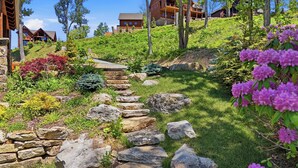 A hillside garden with a stone pathway leading to a wooden cabin. - 3BR LUX Cabin w Firepit, Game Loft + Scenic Views! (Banner Elk)