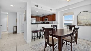 A modern kitchen with wooden cabinets, a central island, and a dining area with a dark wooden table and chairs. - Endless Horizon at the Aruba (Daytona Beach)