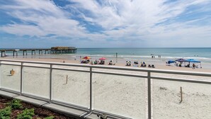 A beach with a pier, umbrellas, and people. - Endless Horizon at the Aruba (Daytona Beach)