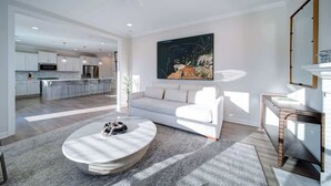 A modern living room with a white sofa, a round coffee table, and a large abstract painting on the wall.
