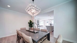 A dining area with a dark wooden table, beige upholstered chairs, and a modern chandelier.