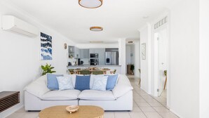 Een moderne woonkamer met een witte bank, een houten salontafel en een keuken op de achtergrond.