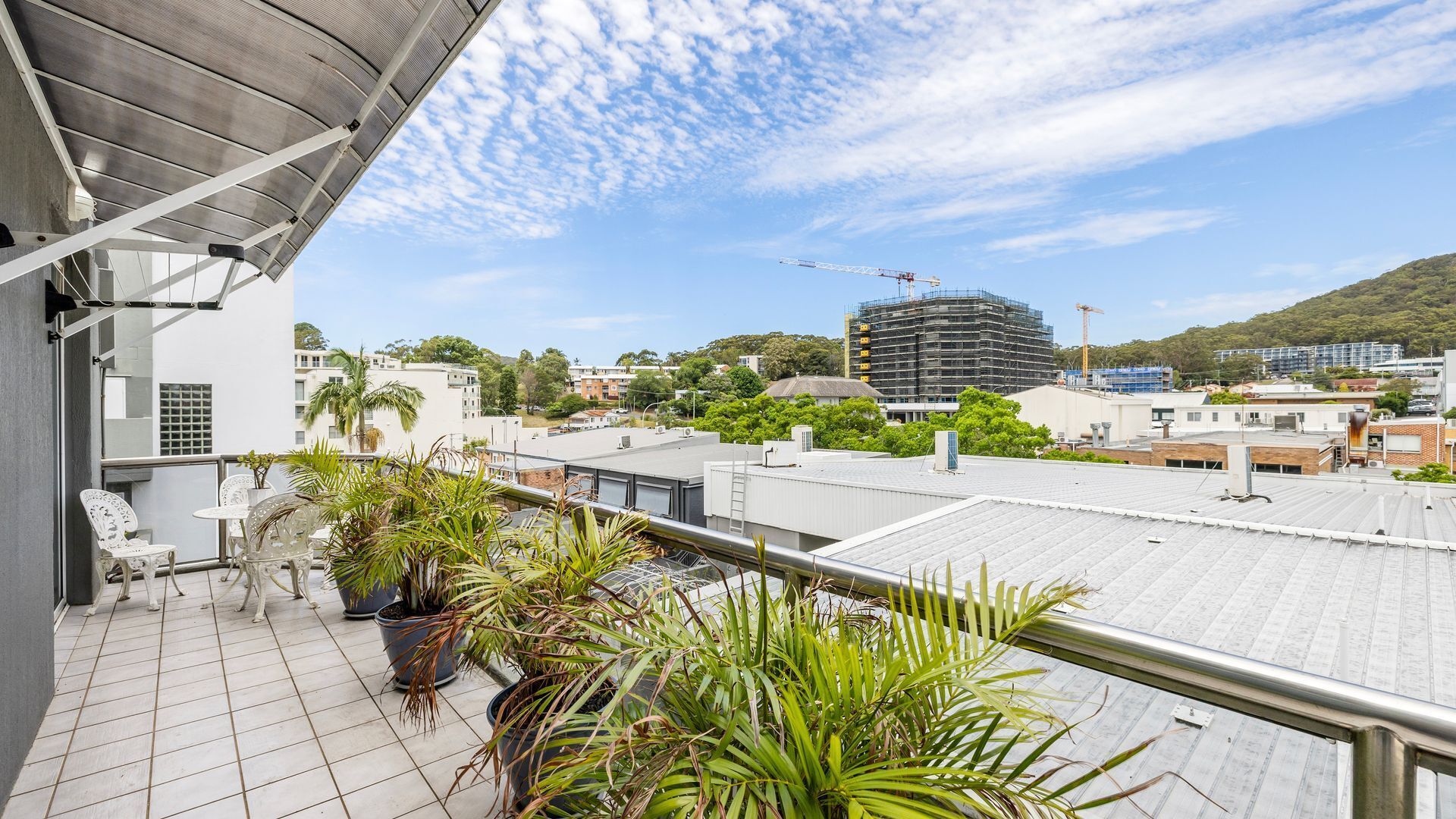A balcony with potted plants, a view of a cityscape, and a construction crane in the distance.