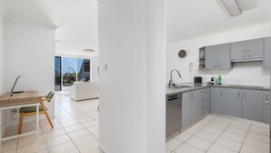 Een moderne keuken met grijze kastjes, een inbouw vaatwasser en een eethoek met een tafel en stoelen.