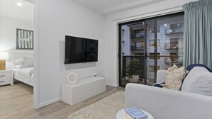 Un salon moderne avec un téléviseur à écran plat, un canapé blanc, une petite table ronde sur laquelle se trouve un livre et une plante en pot.
