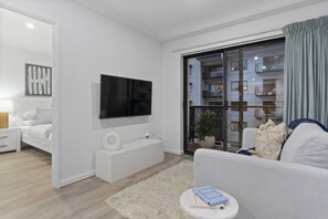 Ein modernes Wohnzimmer mit Flachbildfernseher, einem weißen Sofa, einem kleinen runden Tisch mit einem Buch und einer Topfpflanze.