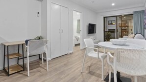 Une pièce moderne et bien éclairée, comprenant un coin repas, des meubles blancs et un téléviseur fixé au mur.