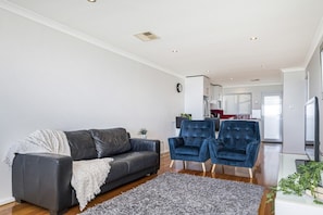 A modern living room with a grey sofa, two blue armchairs, a grey shag rug, and a kitchen in the background. - Renovated Ocean-View Scarborough Apartment | Walk to Beach & Amphitheatre (Scarborough)