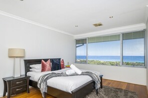 Ein Schlafzimmer mit einem Bett, Nachttischen, einer Lampe und einem Fenster mit Meerblick.