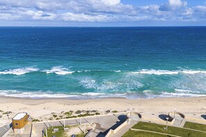 A beach with waves, a clear sky, and a building with a unique design.