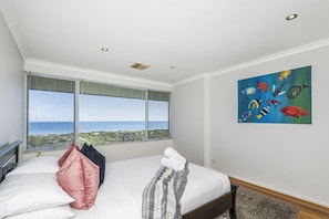 A bedroom with a bed, a painting, a window with a view of the sea, and a ceiling with recessed lighting. - Renovated Ocean-View Scarborough Apartment | Walk to Beach & Amphitheatre (Scarborough)