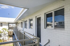 Ein Wohngebäude mit einem überdachten Balkon, einer schwarzen Tür und einem Fenster mit Rollläden.