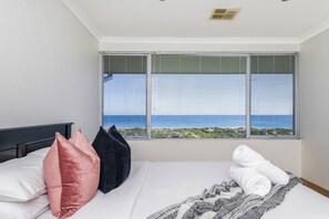 A bedroom with a bed, pillows, a blanket, and a window with a view of the sea.