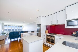 A modern kitchen with white cabinetry, a red accent wall, stainless steel appliances, and a large window providing natural light. - Renovated Ocean-View Scarborough Apartment | Walk to Beach & Amphitheatre (Scarborough)