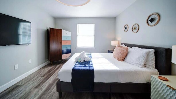 A modern bedroom with a large bed, a flat-screen TV, a wardrobe, and a window.