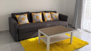 Ein modernes Wohnzimmer mit einem grauen Sofa, gelb-weißen Blumenkissen, einem weißen Couchtisch und einem leuchtend gelben Teppich.