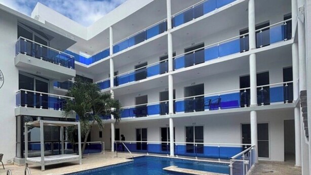 A multi-story hotel with a central swimming pool, balconies with glass railings, and a palm tree. - Fantastic 2-bedroom apartment with AC in charming Sosúa (Sosúa)