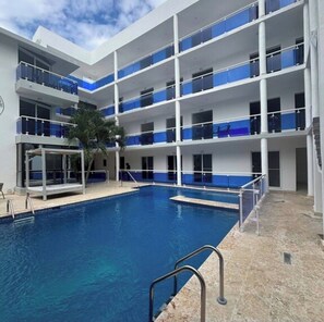 A multi-story hotel with a central swimming pool, balconies with glass railings, and a palm tree. - Fantastic 2-bedroom apartment with AC in charming Sosúa (Sosúa)