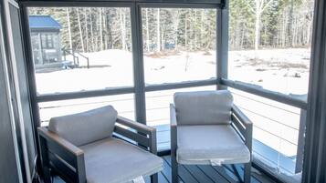 Un espace extérieur abrité, aménagé avec deux chaises et une table, offrant une vue sur un paysage enneigé.