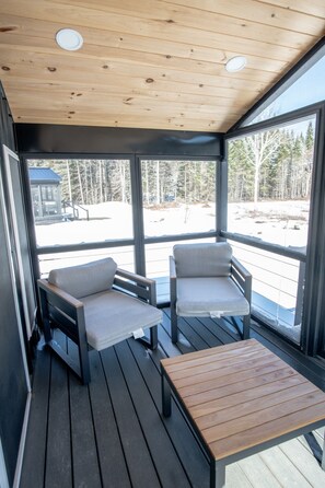 Ein überdachter Außenbereich mit zwei Stühlen und einem Tisch mit Blick auf eine verschneite Landschaft.