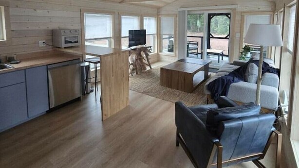A spacious living area with a wooden ceiling, a kitchen with modern appliances, and a comfortable seating area with a sofa and chairs.