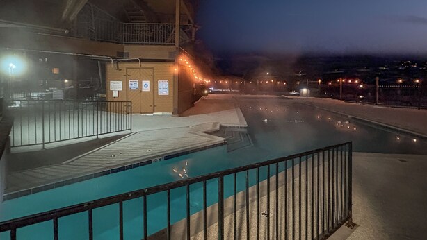 A heated outdoor pool area with a metal railing, a covered seating area, and a view of a distant town at night. - The Grand Duplex of Silvercreek Inn. Combination of two lock off units. (Granby)