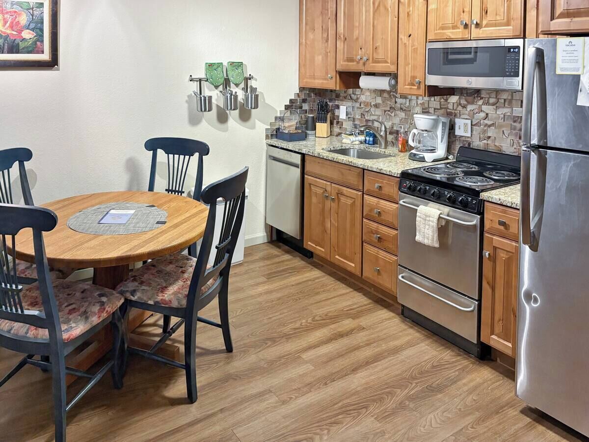 Une cuisine dotée de meubles en bois, d’un réfrigérateur en acier inoxydable, d’un four à micro-ondes, d’une cuisinière et d’une table à manger avec des chaises.